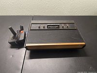 Top-down view of Atari 2600 console and joystick on a black table surface against a light wall.