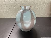 Front and side view of round glass vase with swirled pastel blue and brown colors on a dark surface.