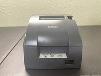 Front right angle view of Epson TM-U220B printer showing power switch, paper feed slot, and Epson logo.