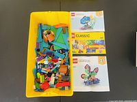 Yellow plastic bin filled with assorted Lego bricks and three distinct Lego instruction booklets placed on the side