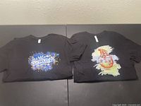 Two black t-shirts laid flat side by side showing front graphic designs
