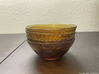 Side profile view of a single amber vintage glass dish bowl showing intricate etched patterns and translucent amber color.
