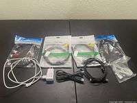 9 cords arranged on table, 4 sealed printer to USB cords in retail packaging, various black and white cables, white Android charger with wall plug included