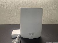 Front view of the white Netgear Orbi RBR50 router with power adapter placed behind it.