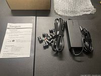 Photo showing Targus instruction manual, power adapter, power cord, and multiple interchangeable tips laid out side by side on a black surface.