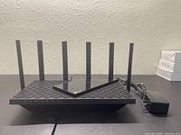 TP-Link Archer AX73 router with eight antennas and power cord, angled front view on black surface.