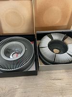 Two Kodak Carousel slide trays inside boxes; one gray Kodak Carousel 140 Slide Tray and one black Yankee C-80 Rotary Slide Tray