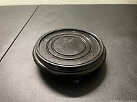 Top view of the round wooden stand with concentric carved rings; visible wear and scratches.