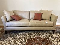 Front view of beige herringbone sofa with four decorative pillows on patterned rug