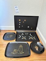 Full set of five black lacquer serving trays with various artistic designs grouped on floor.