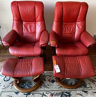 Front view of two red leather recliner chairs with matching footstools on wood swivel bases