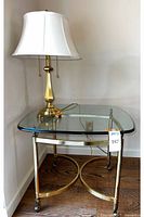 Full view of the brass lamp sitting on the brass framed glass-top end table placed in a corner.