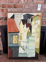 Front view of framed canvas painting showing buildings with pointed roofs and windows.
