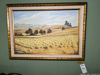 Full view of the framed landscape painting showing fields, trees, and distant hills under a partly cloudy sky.