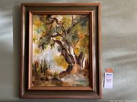 Framed painting showing a large tree in a landscape scene with natural warm colors