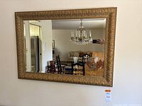 Full view of the rectangular mirror with gold ornate gilt frame hanging on the wall reflecting room interior