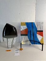 Photo of two glass art pieces: a La Murrina Murano glass vase with black tinted top and clear bottom, alongside a colorful glass plate mounted on a black stand.