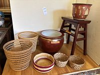 Wide view of the entire lot including two large woven baskets, three smaller baskets, the large ceramic pot on the floor, smaller decorative pot with Chinese figures on wooden stand.