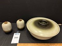 Front view of casserole dish with lid and salt and pepper shakers on black background alongside ruler and lot tag