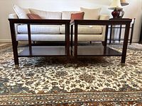 Pair of dark wood side tables side by side on a patterned carpet in front of a beige sofa