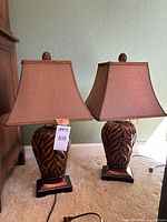 Pair of table lamps with carved wood bases and square brown fabric shades on carpeted floor.