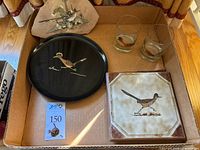 Box containing Couroc round serving plate with roadrunner design, two clear glass tumblers, ceramic pot holder with roadrunner, metal roadrunner charm on card, and a painted sandstone piece with roadrunner and desert scene