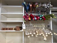 Shelving rack with cream satin hangers below and brightly colored padded corduroy hangers in jewel tones above on two rods