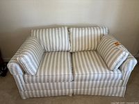 Front view of loveseat showing cream and neutral vertical striped fabric upholstery with cushions and pillows.