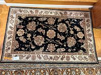 Full view of the silk and wool rug showing black background with beige and maroon floral motifs and cream border.