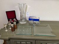 Overall view of sterling silver salt and pepper shakers, tall fluted vase, two square glass platters, and small cream and sugar set in original box.