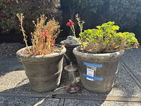Two cement pots with plants and hummingbird feeder between them on paved surface