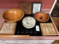 Full lot showing all items on countertop including two wooden bowls, earthenware casserole dish with lid, four ceramic tiles mounted in wooden frames, small cutting board, and ruler for size reference.