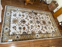 Full view of the wool area rug showing cream background with intricate floral and geometric brown and blue designs laid on a wood floor.