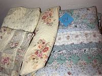 Two floral pattern quilts and one sham stacked and folded showing various floral designs and colors