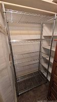 Front view of a 5-shelf metal wire rack in a narrow room, showing wire mesh shelves and silver poles.