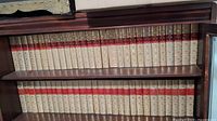 Photo showing the full collection of 57 hardcover books arranged on wooden shelves, displaying uniform beige covers with red and gold embossed spines.