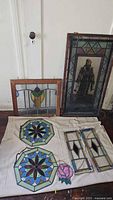 Photo showing full set of stained glass windows arranged on the floor, including large rectangular panel with figure, octagonal panels, small rectangular panels and rose-shaped piece.