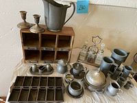 Full view of lot on table with wooden cubby, pewter pitcher, silver-plated candlesticks, various small metal containers and trays.