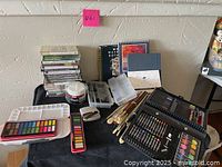 Overall photo of artist kit showing instructional DVDs, botanical painting instruction book, paint palettes with vibrant colors, brushes, palettes, and tools