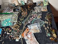 Photo showing assortment of jewelry including bead necklaces, pendants, and small bags of beads and findings on black cloth.