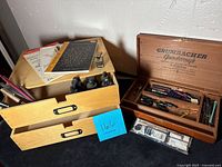 Two light wood drawers filled with various calligraphy nibs, ink bottles, and manuals, alongside a wooden box labeled Grumbacher Gainsborough containing more calligraphy supplies.