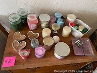 Overview photo showing multiple candles including jar candles, pillar candles, heart-shaped candles, and tealights arranged on a wooden table.