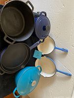 Top view of cast iron skillets and enameled pots with lids showing navy blue, teal, and blue cream interiors.