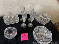 Full view of all crystal items on black cloth: three champagne glasses, two serving bowls, covered butter dish, small bowl