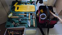 Overall view of gardening tools organized in green plastic storage case and red soft-sided bag with gloves and accessories