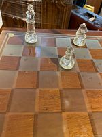 Glass chessboard with some chess pieces placed on it showing frosted and clear squares and chess pieces.
