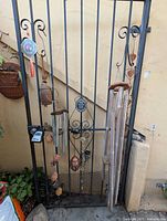 Full view of gate with various hanging garden decor items: Feng Shui mirror, vintage bell, multiple wind chimes, and hanging crystals.