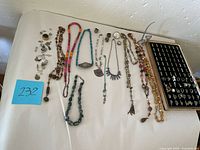 Full overview of costume jewelry lot with necklaces, rings, charms, and earrings arranged on a white surface.