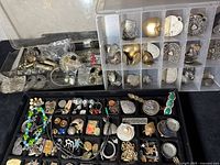 Overview of jewelry pieces in a tray showing assorted metal pendants and earrings in silver and gold tones.