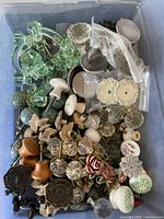 Top-down view showing a large assortment of vintage knobs and pulls of various materials and styles including glass, ceramic, metal, and painted designs.